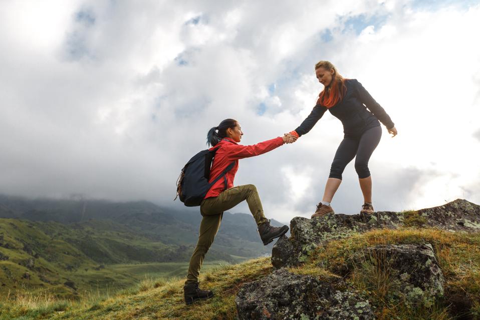 Girls helping each other hike up a mountain at sunrise. Giving a helping hand, and active fit lifestyle concept.