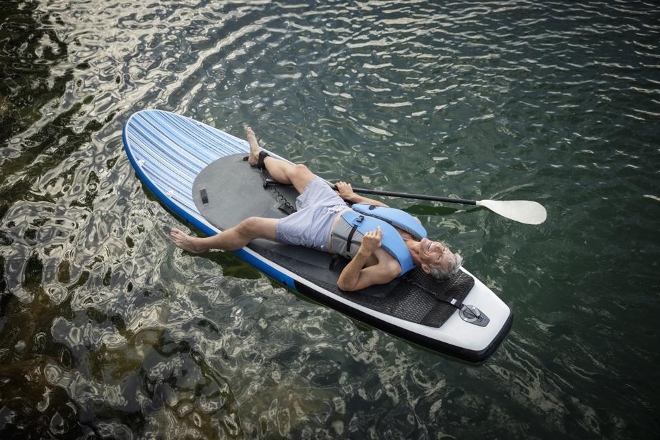 Serene mature man relaxing, laying on paddleboard on lake