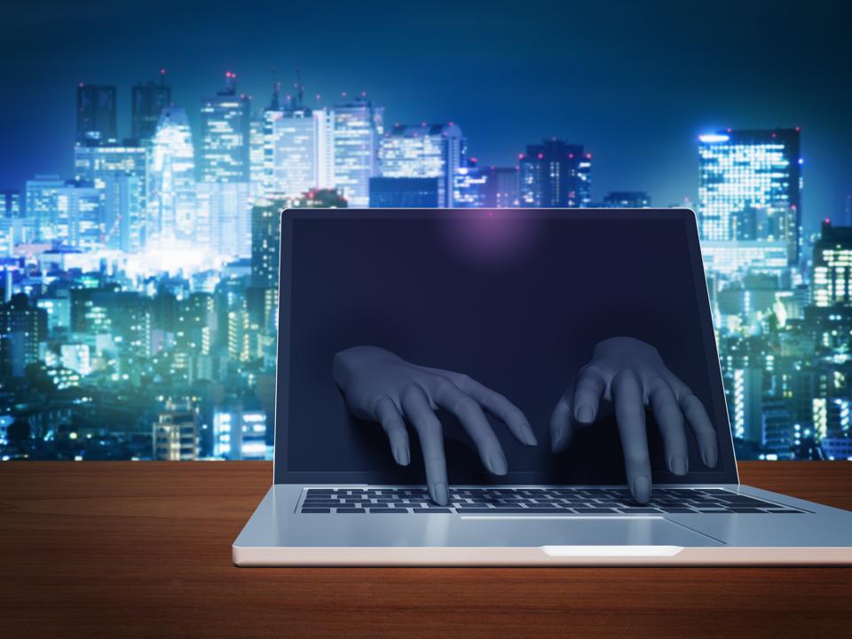 Hacker's hand to operate keyboard from laptop computer monitor