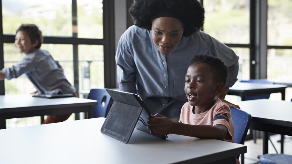 Teacher assisting boy working tablet at school