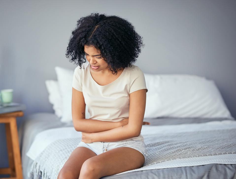 Shot of a young woman suffering from stomach cramps in her bedroom