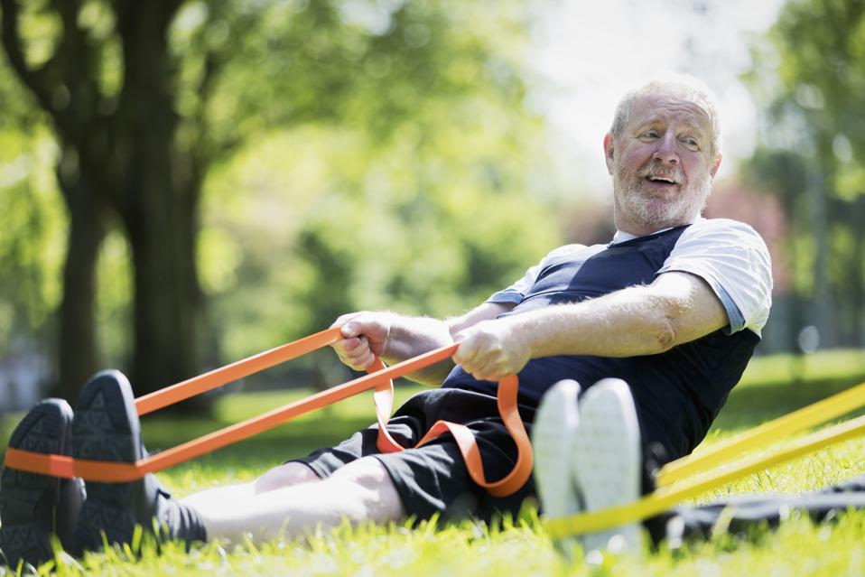Active senior man exercising in park, stretching with resistance band