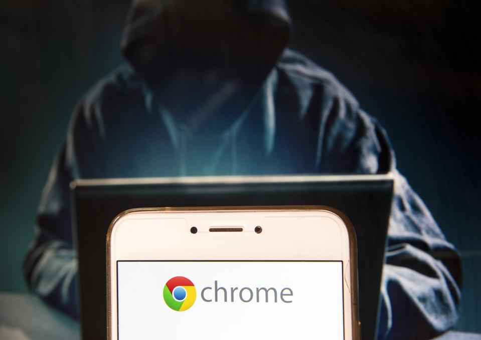 Google Chrome logo is seen displayed on an Android mobile device with a figure of hacker in the background. 