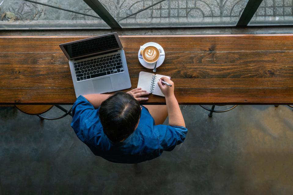 A young woman with a laptop and a latte looking out a cafe window.