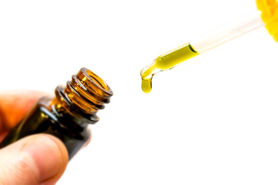 Hand holding bottle of CBD oil in pipette isolated