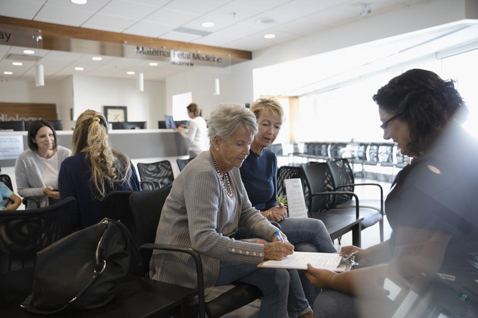 Female nurse discussing insurance paperwork with senior patient in clinic waiting room