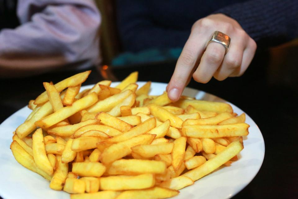 A hand reaching to pick up a french fry from a plate