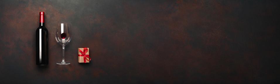 Bottle of wine with wineglass and gift box on rusty brown background. Panoramic top view with space for your text