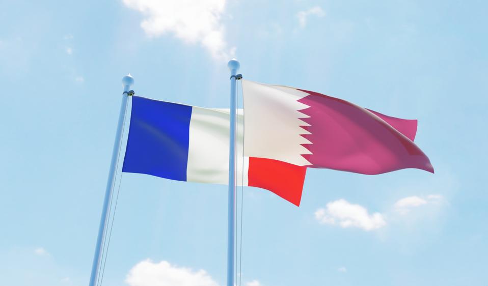 Qatar and France, two flags waving against blue sky