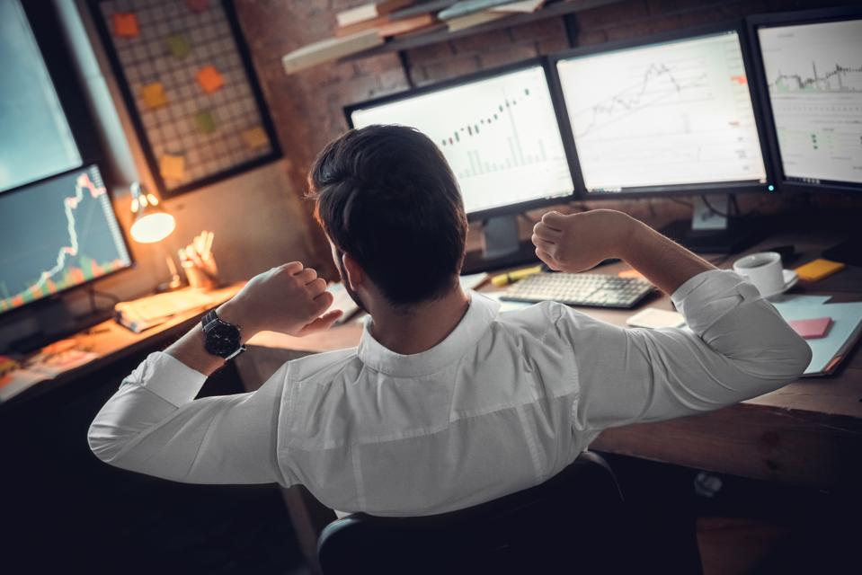 Rear view at stock trader broker stretching hands at workplace