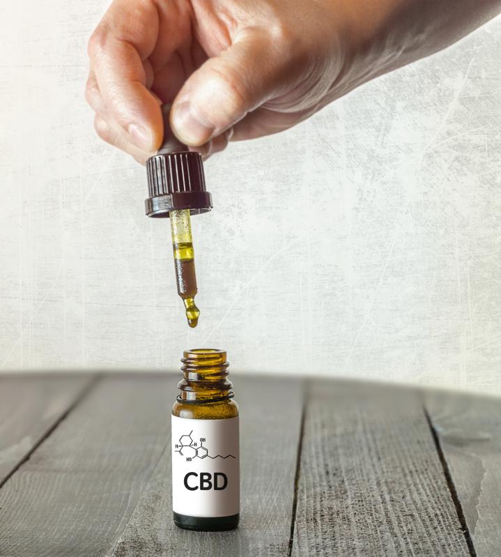 Hand holding pipette with CBD oil on wooden table