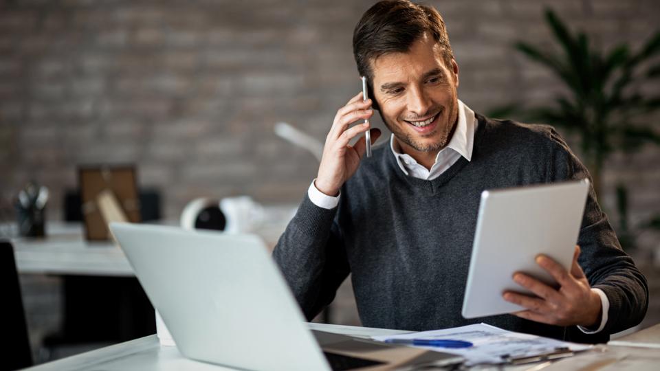 Happy businessman using digital tablet while talking on cell phone in the office.