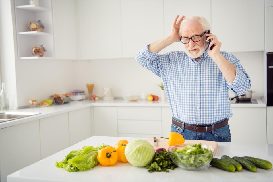 Close up portrait grey haired he his him grandpa hold head hand arm telephone smart phone wrong recipe listen new worried wear specs casual checkered plaid shirt jeans denim outfit light kitchen
