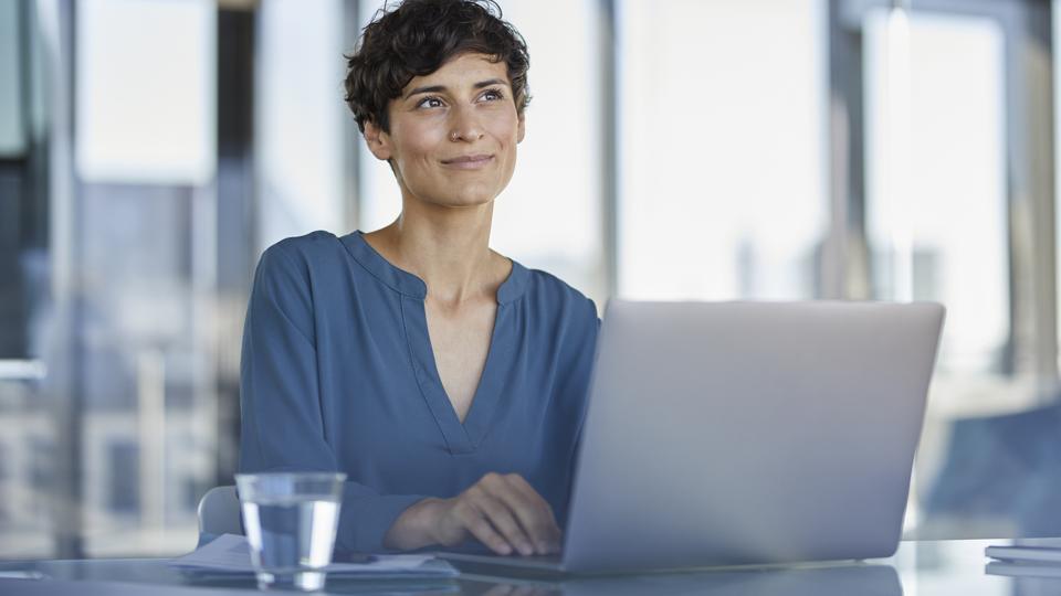 Smiling businesswoman sitting at desk in office with laptop