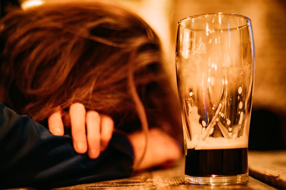 Young drunk woman sleeping on bar counter drinking dark beer