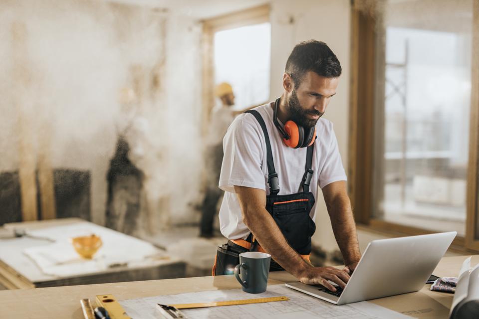Young manual worker working on a computer at construction site.