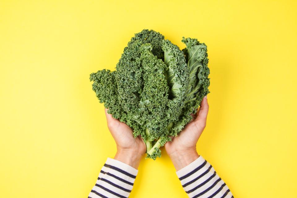 Cropped Image Of Woman Holding Kale Against Yellow Background