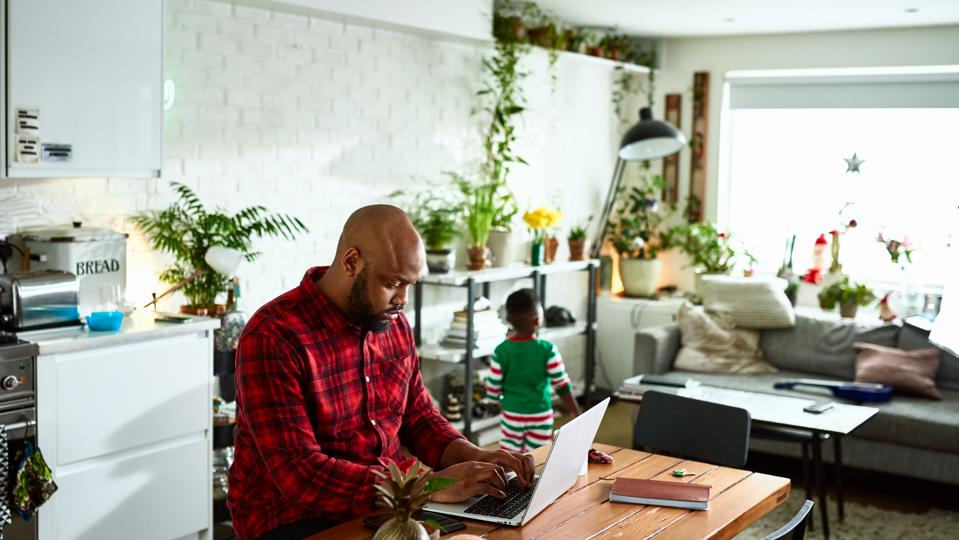 Padre trabajando desde casa en la computadora portátil y cuidando a su hijo
