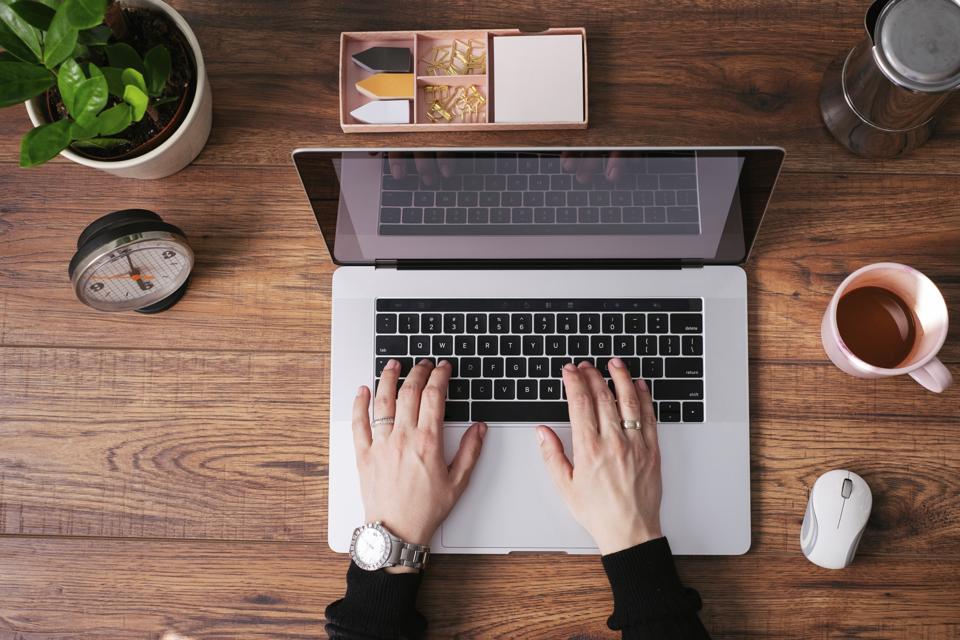 Woman's hands working on laptop at home office, top view