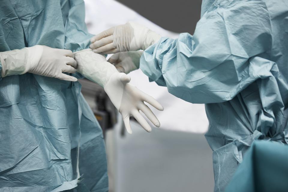 Female doctor helping surgeon wearing glove