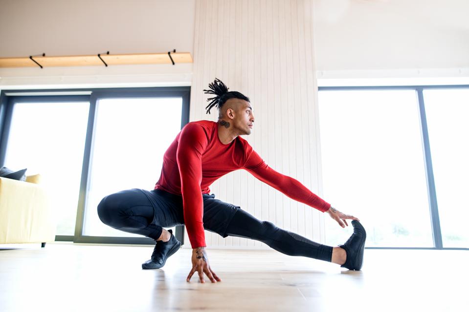 ett porträtt av fit blandad ras man med dreadlocks gör träning hemma, stretching.