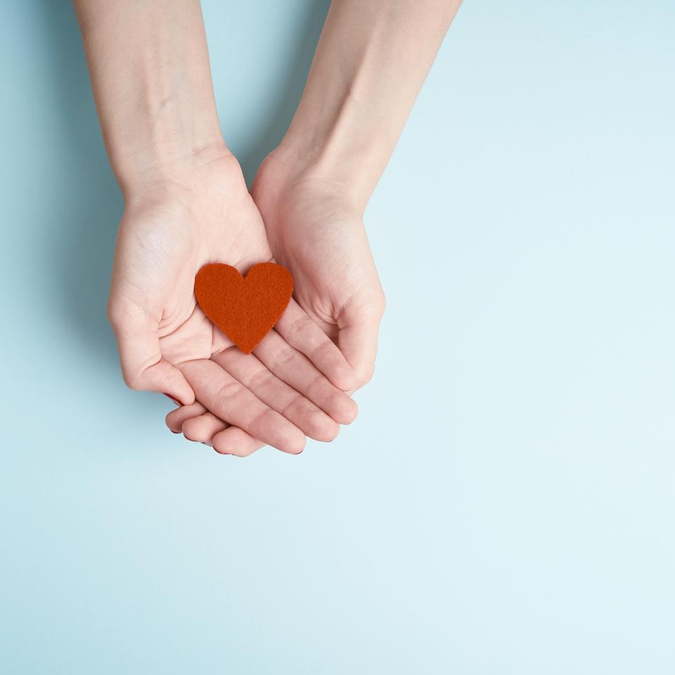a person holding red heart in hands, donate and family insurance concept, on aquamarine background, copy space top view
