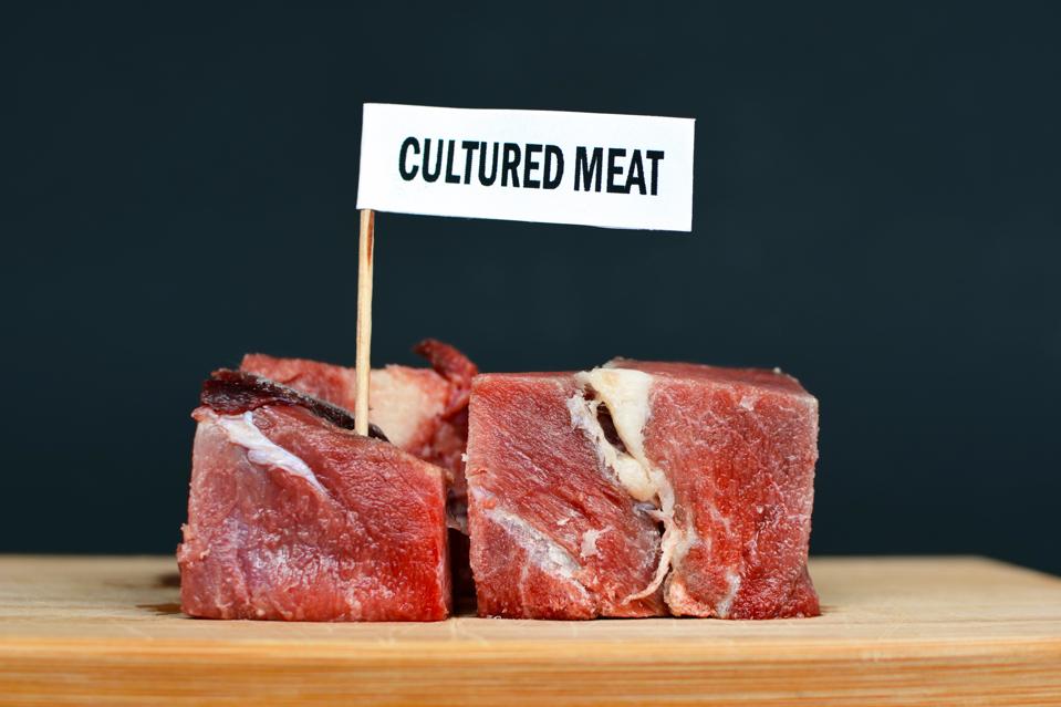 Big raw red meat chunks on wooden plate with label saying 'cultured meat', concept for artificial meat production