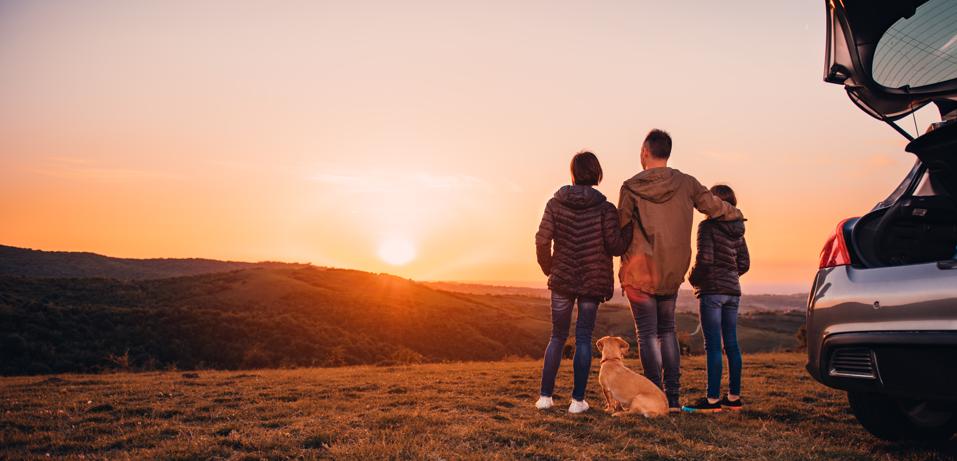 Family with dog hugging on the hill and looking at sunset