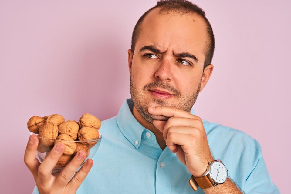 Young man holding bowl with walnuts standing over isolated pink background serious face thinking about question, very confused idea