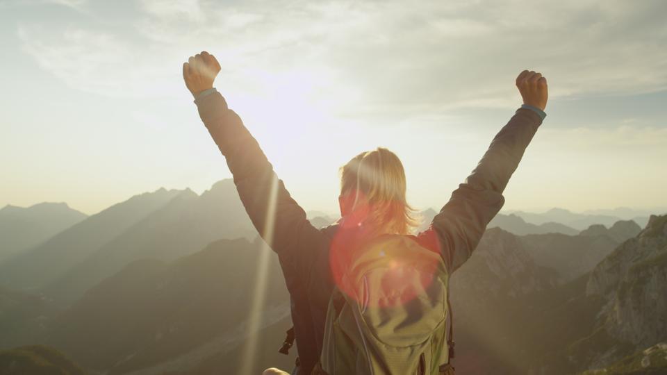 LENS FLARE: Golden sun rays shine on young couple hiking up a steep hill in Alps