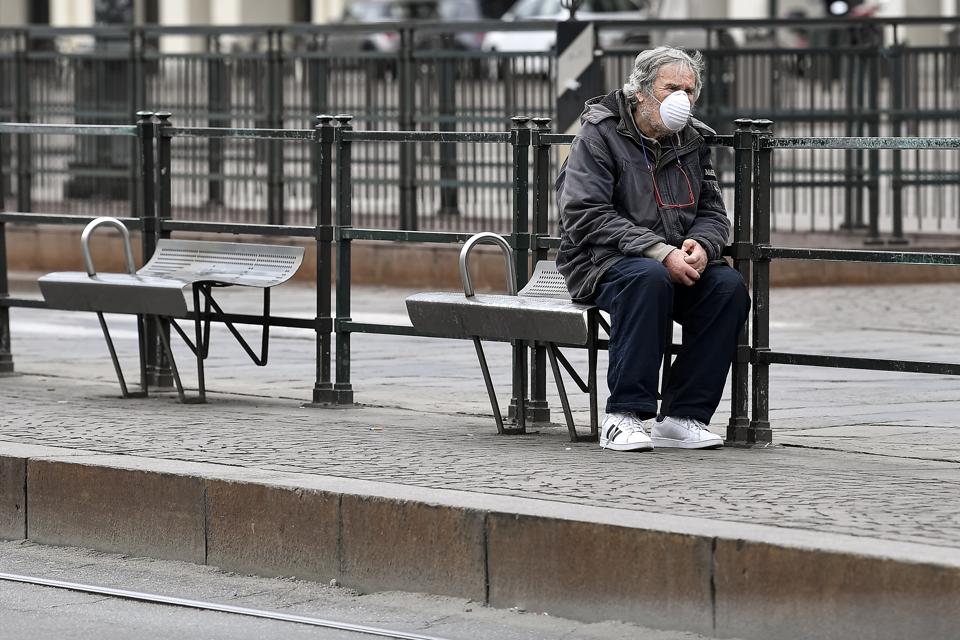 A man wearing a respiratory mask waits at bus stop. The...