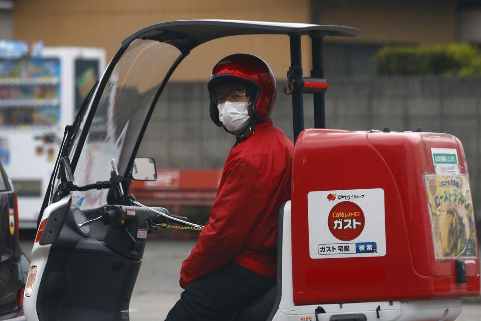 A food delivery man looks on while wearing a face mask as a...