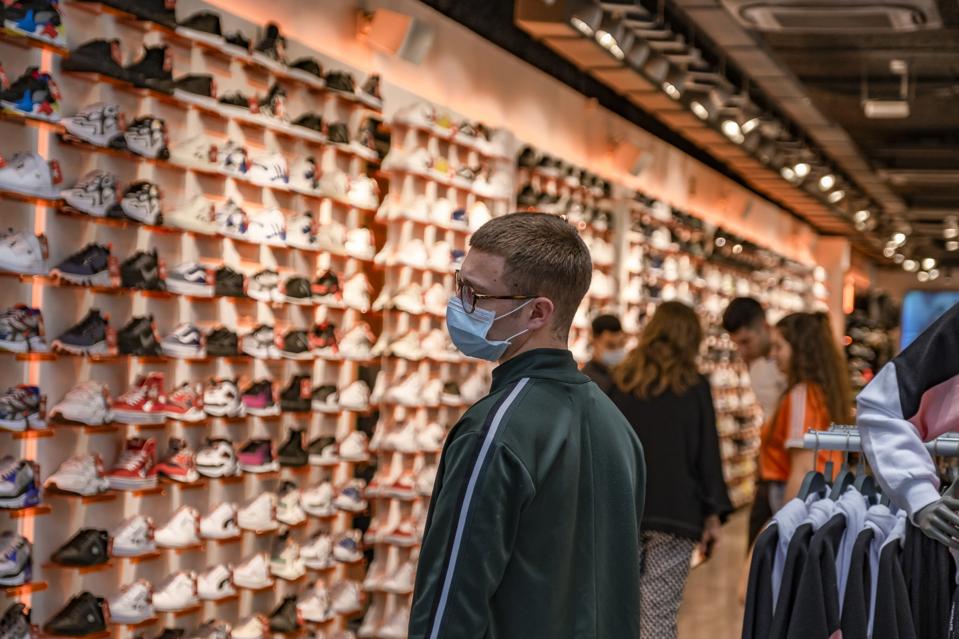A man shopping at a shoe store while wearing a face mask as...