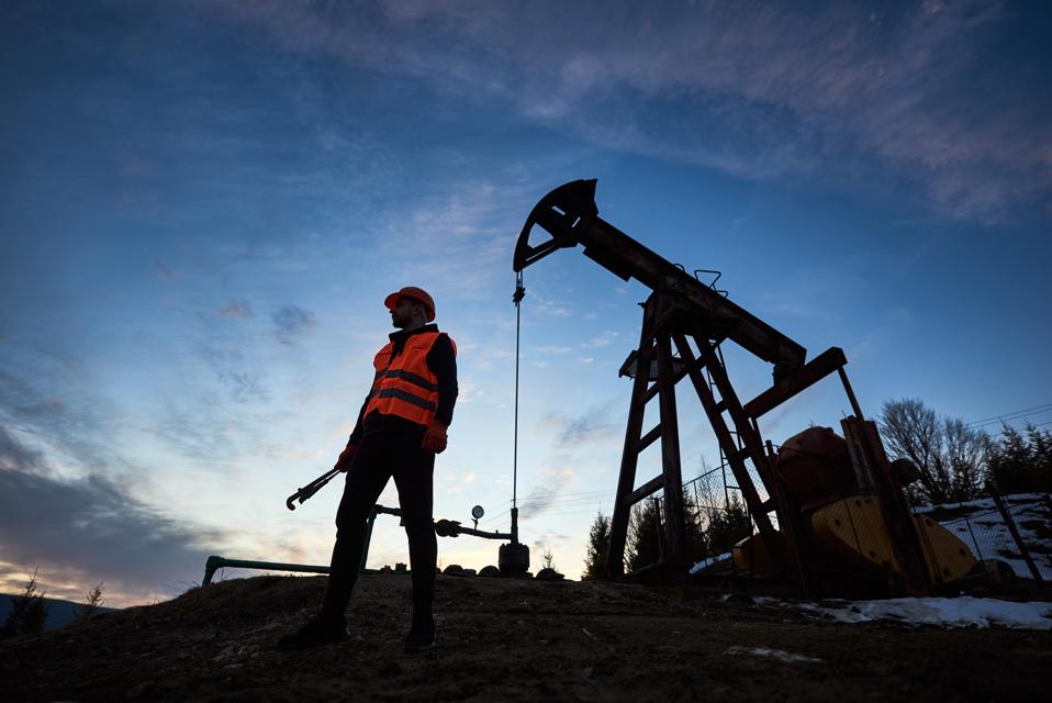 Silhouette of a worker and an oil pump jack on the sunset agains beautiful sky