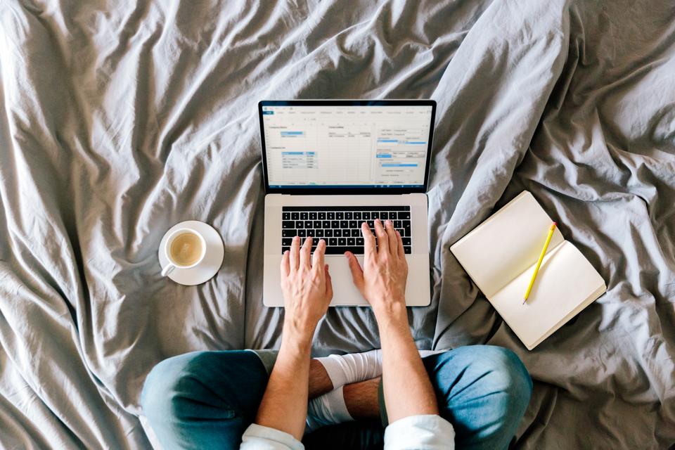 Overhead view of a man working on a laptop from his bed at home