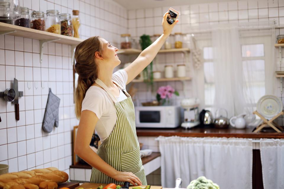 The young female broadcast live VLOG social media and selfie photo in the kitchen room while working from home. COVID-19