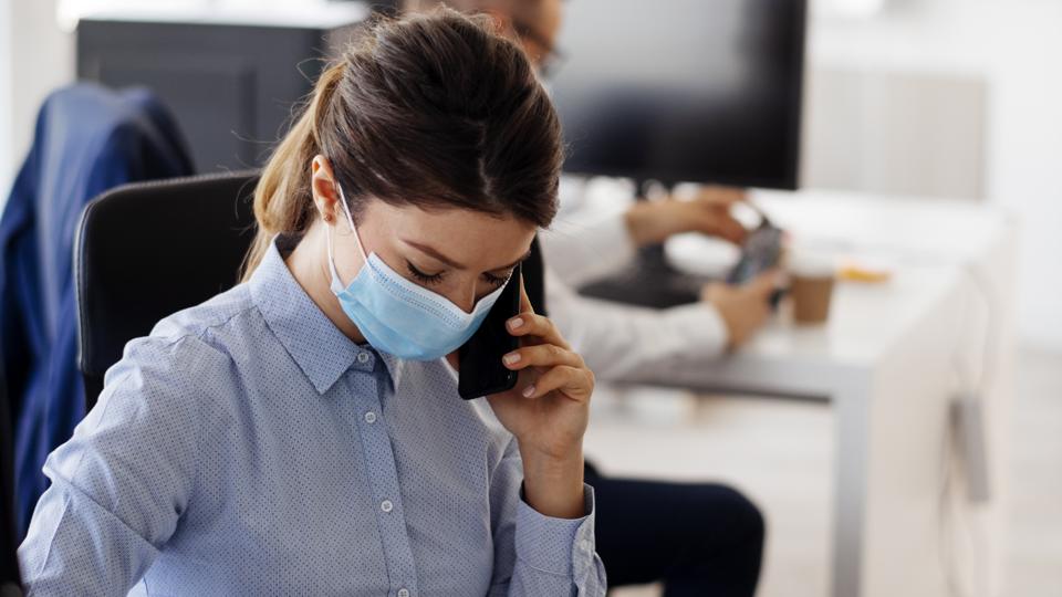 Young businesswoman with face mask talking on the phone while working.