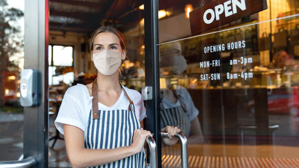 Happy business owner opening the door at a cafe wearing a facemask