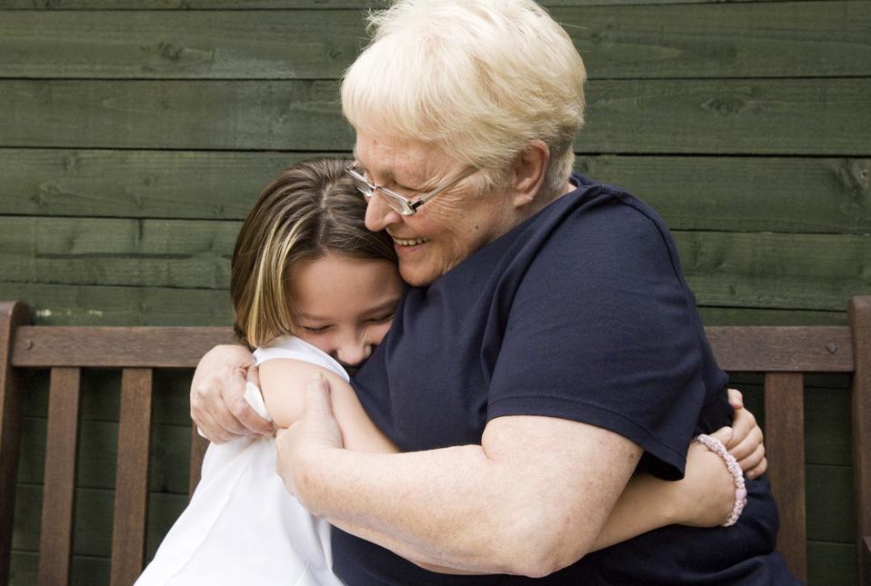 Senior woman hugging granddaughter on bench outdoors