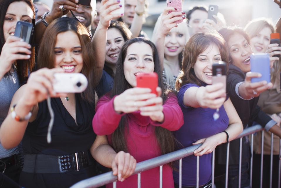 Fans taking pictures with cell phone behind barrier