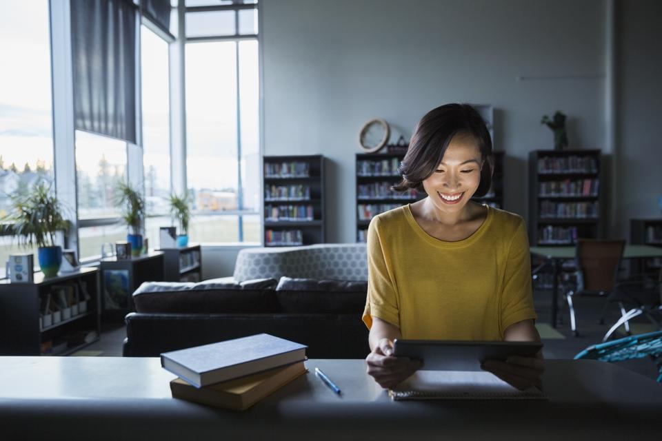 Smiling teacher using digital tablet in dark library