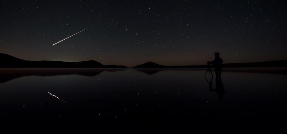 A bright meteor flying past the Big Dipper reflected on a lake.