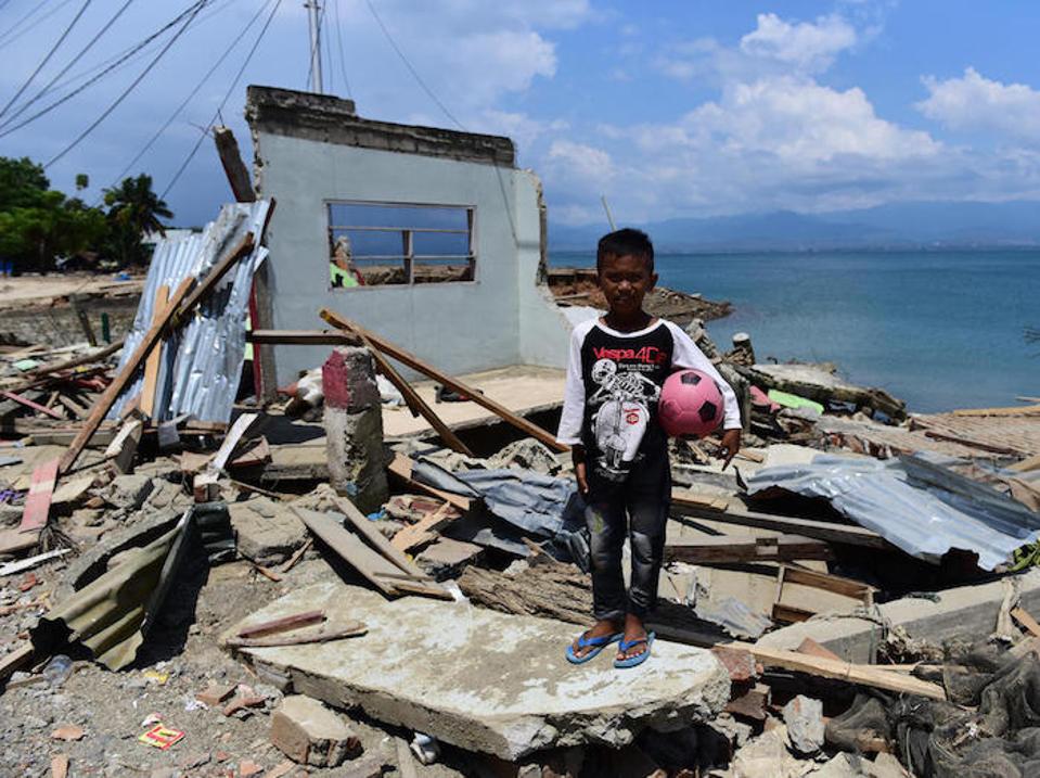 On October 3, 2018, 10-year-old Rido Saputra stands in front of the ruins of his home, destroyed by a tsunami in Donggala Regency, Central Sulawesi, Indonesia.