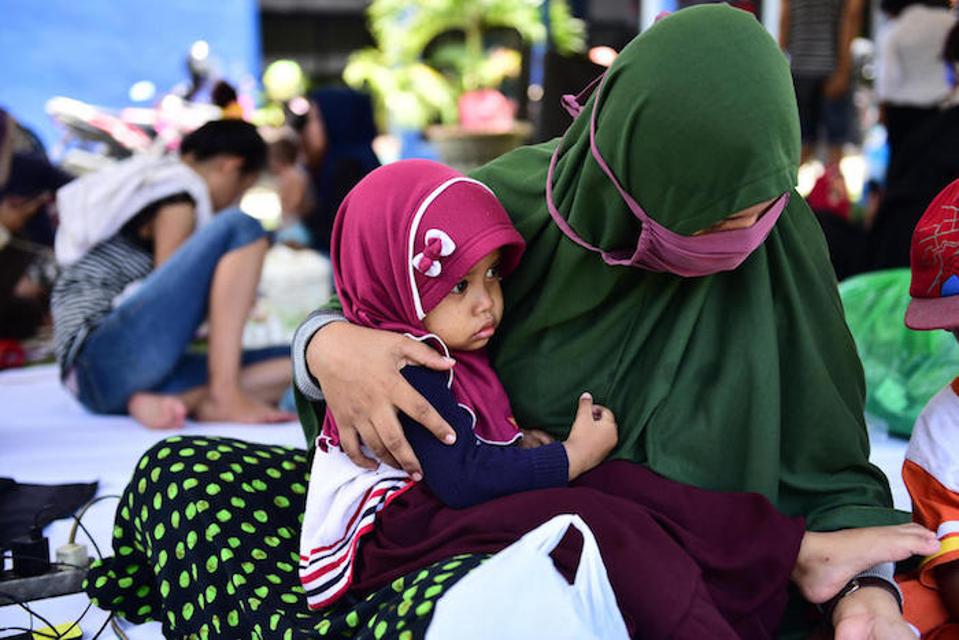 On October 2, 2018 in Indonesia, 2-year-old Fatimah sits on her mother's lap in the evacuation tent yard of the RRI office, East Lolu, Palu City, Central Sulawesi.