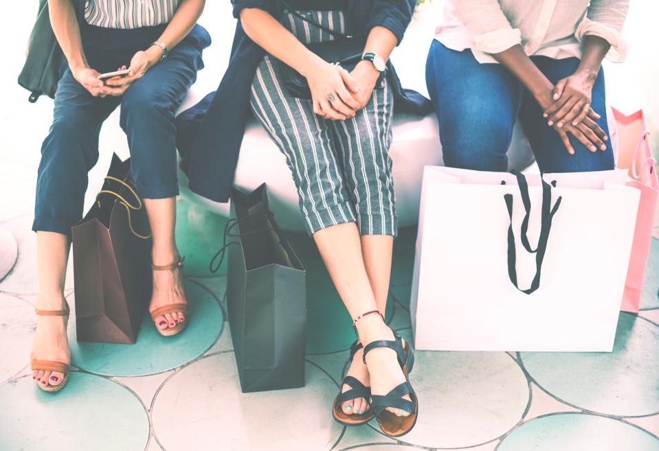 Closely cropped stock image of three women sitting down with shopping bags at their feet.