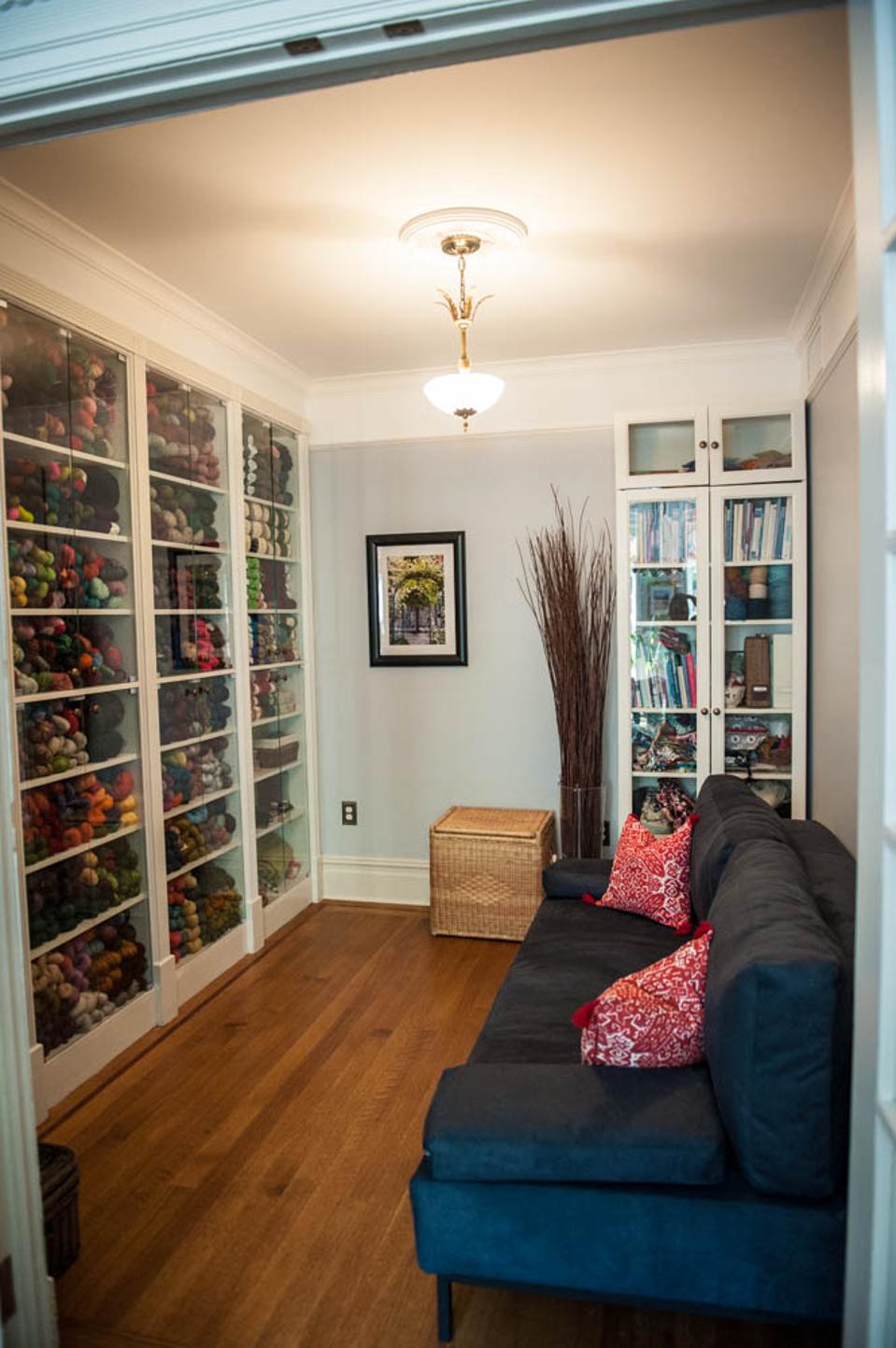 A room with shelves of yarn and a blue sofa.
