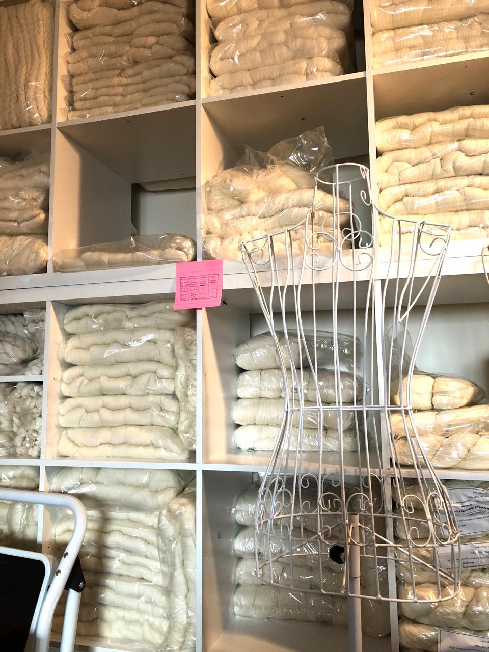 Shelves of un-dyed yarn and a metal dress form.