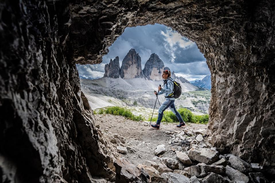 Woman hiking, seen through a circle in rock, in mountainous area.