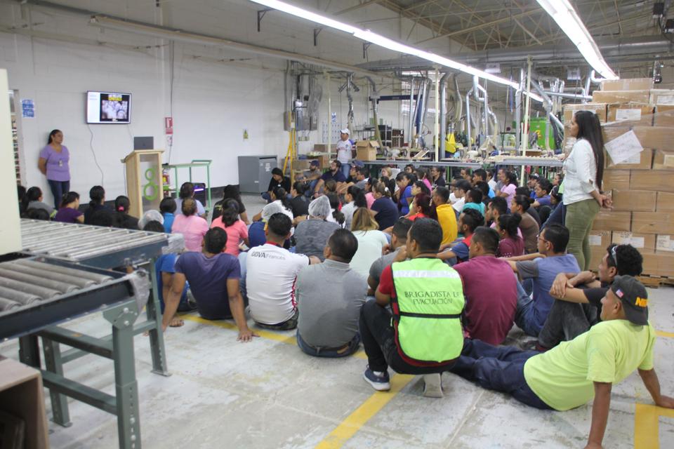 Photo of a manufacturing plant with 100 people seated on the floor participating in a meeting.