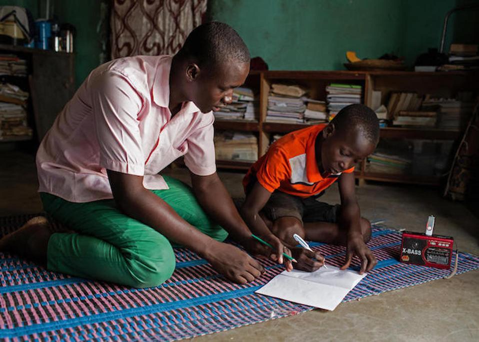 Sa Dori, Burkina Faso, ang facilitator ng paaralan sa radyo na si Abdoulaye, 23, ay tumutulong sa 14-taong-gulang na si Hussaini sa pamamagitan ng mga aralin na broadcast bilang bahagi ng programa ng Edukasyon sa suportang Radio sa UNICEF na sinusuportahan